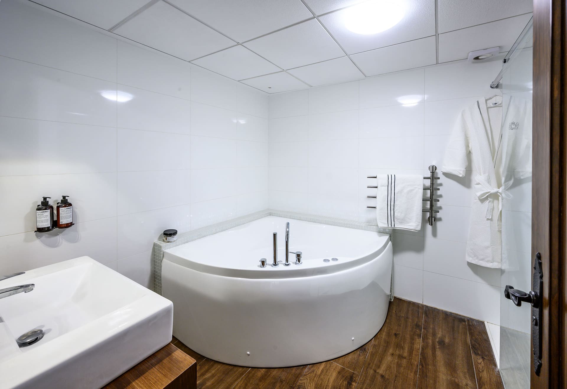 The bathroom with a corner jacuzzi and a bathrobe ready on the wall.