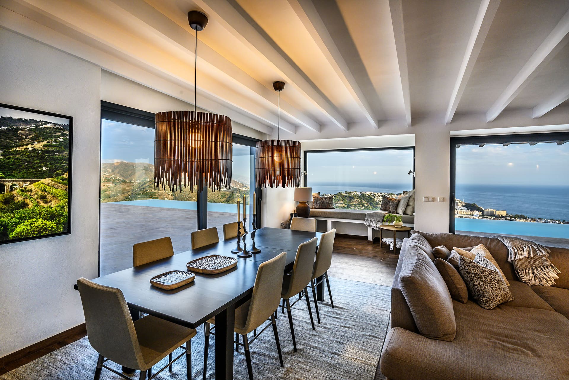 The dining and living room at El Cortijo, pendant lights over the table and the sea through the windows.