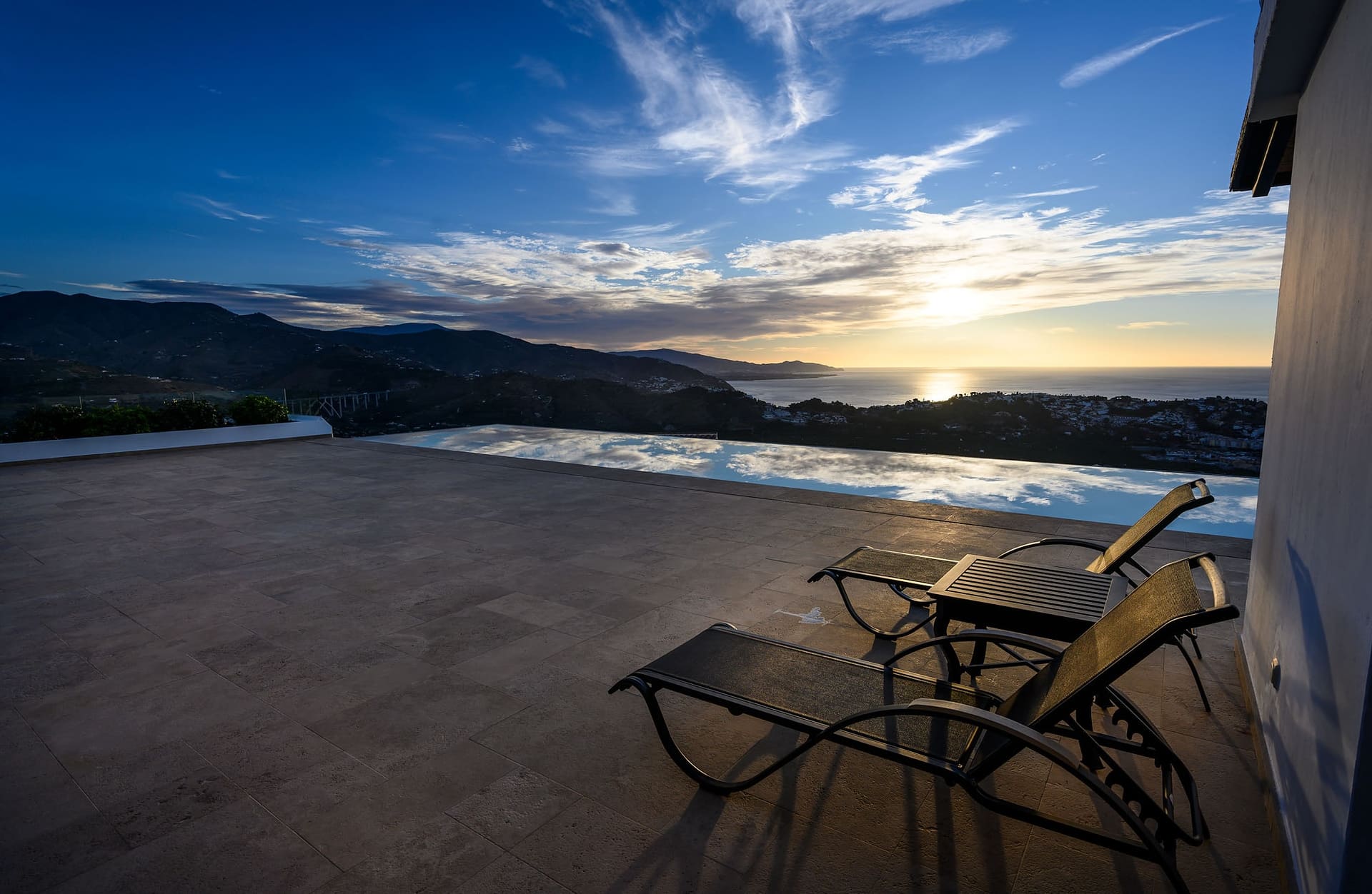 Two loungers on the terrace at sunset, the infinity pool and the sea beyond.