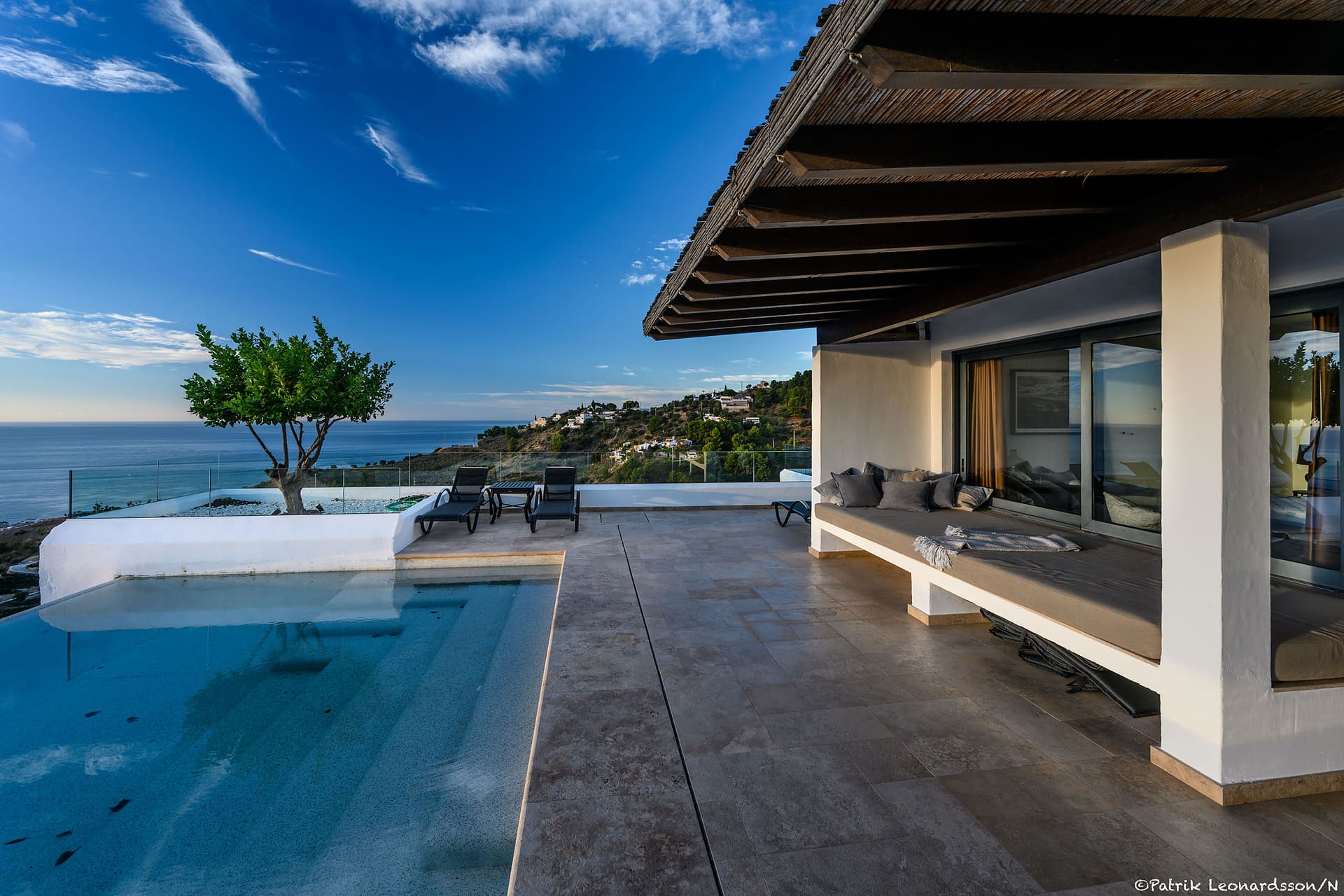 The pool running alongside the covered terrace, an olive tree at its far end and the sea beyond.