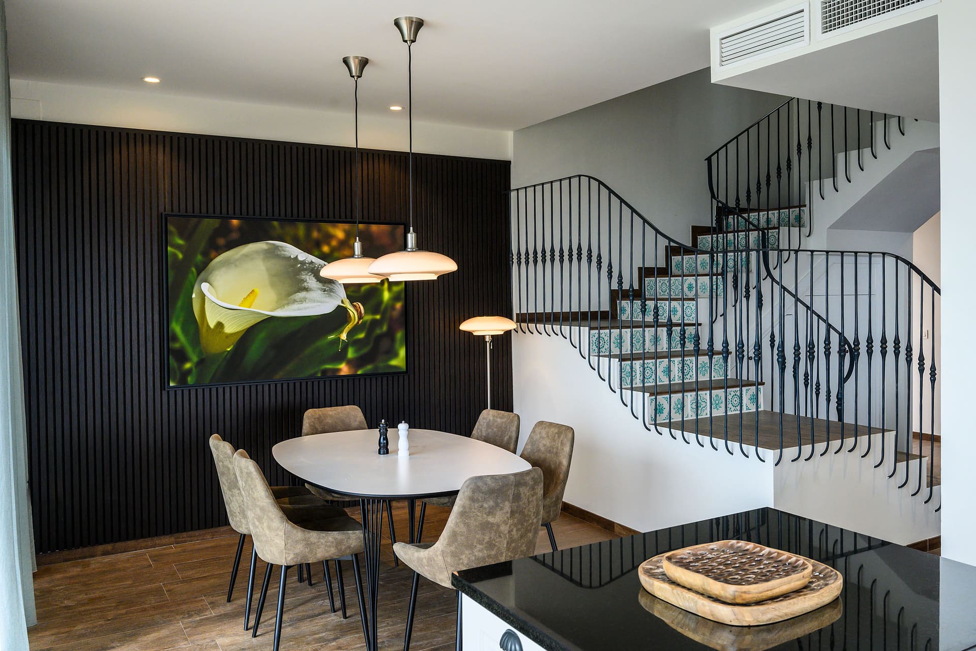 A round dining table beneath pendant lights, the wrought-iron staircase beside it.