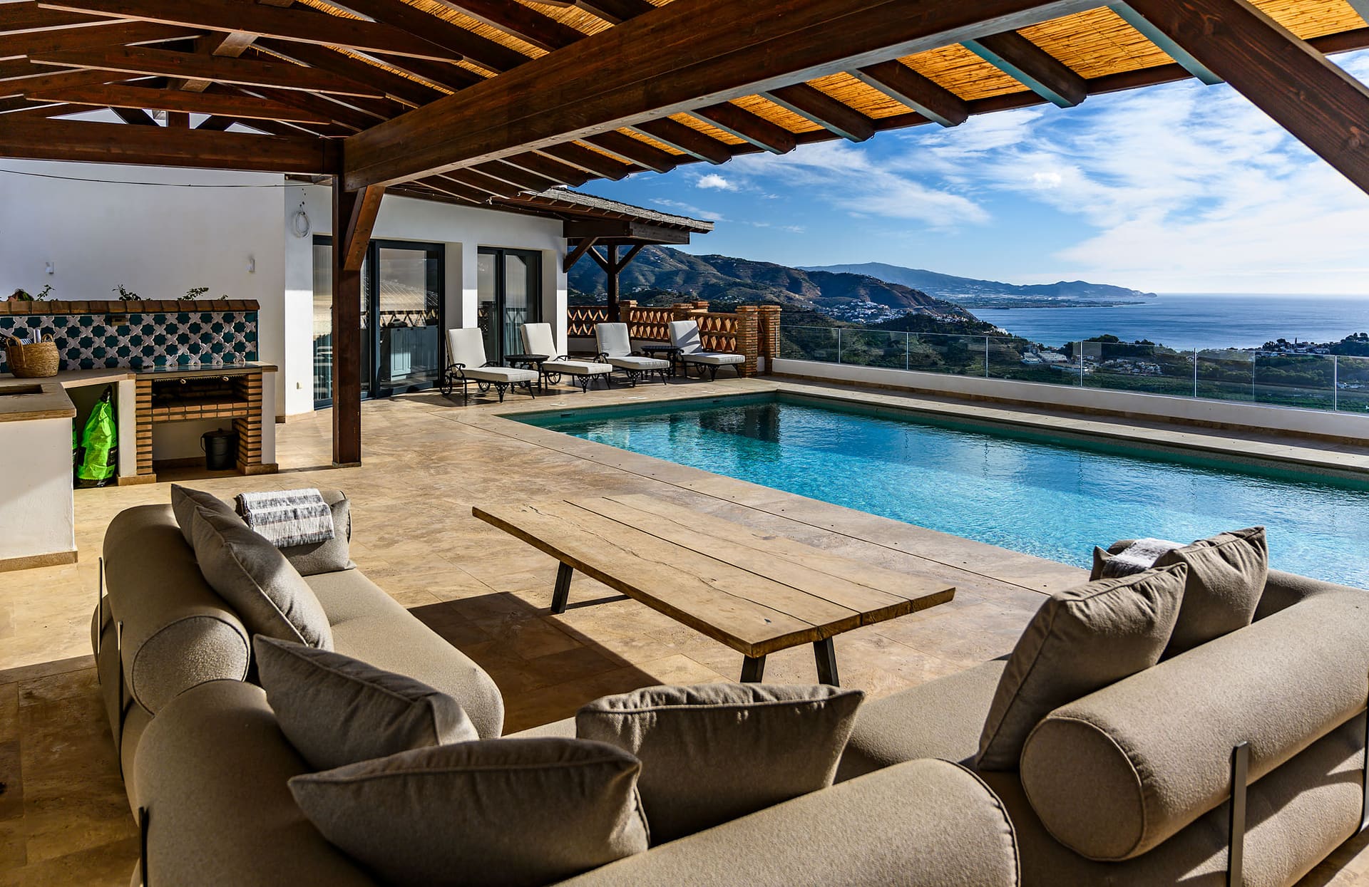 Sofas under the pergola by Villa Limón's pool, the coast stretching away beyond.