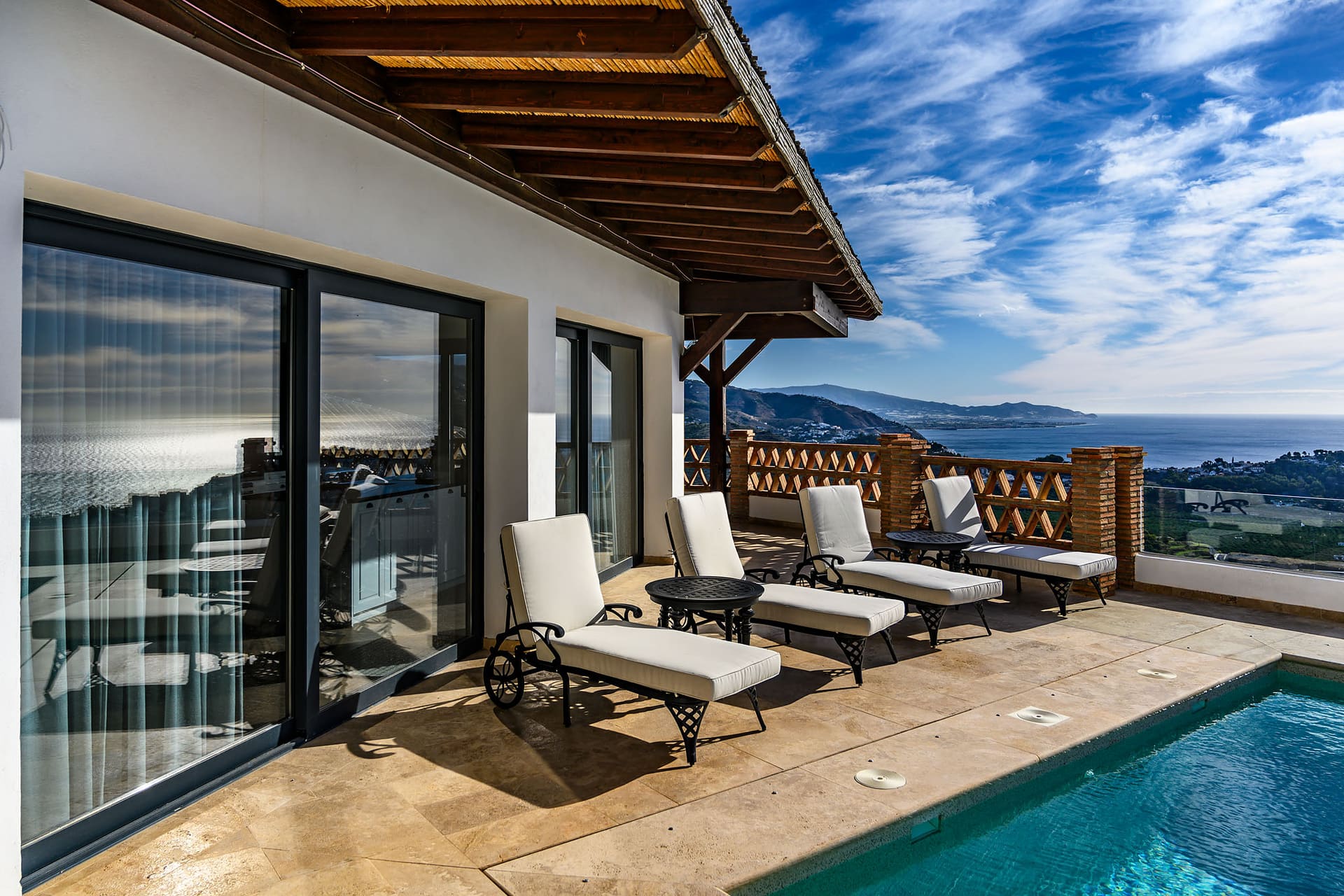 Loungers beside Villa Limón's pool, the house behind and the coast in the distance.