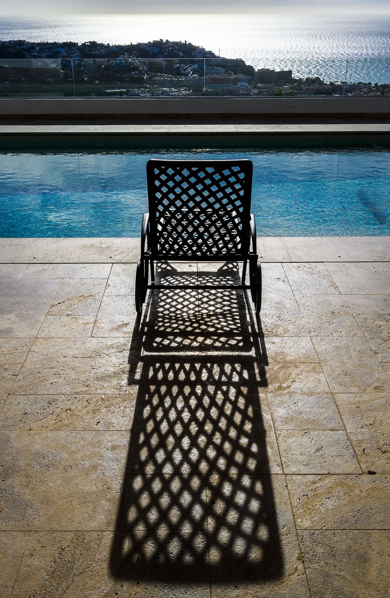 A wrought-iron lounger by the pool casting a long shadow, the sea beyond.