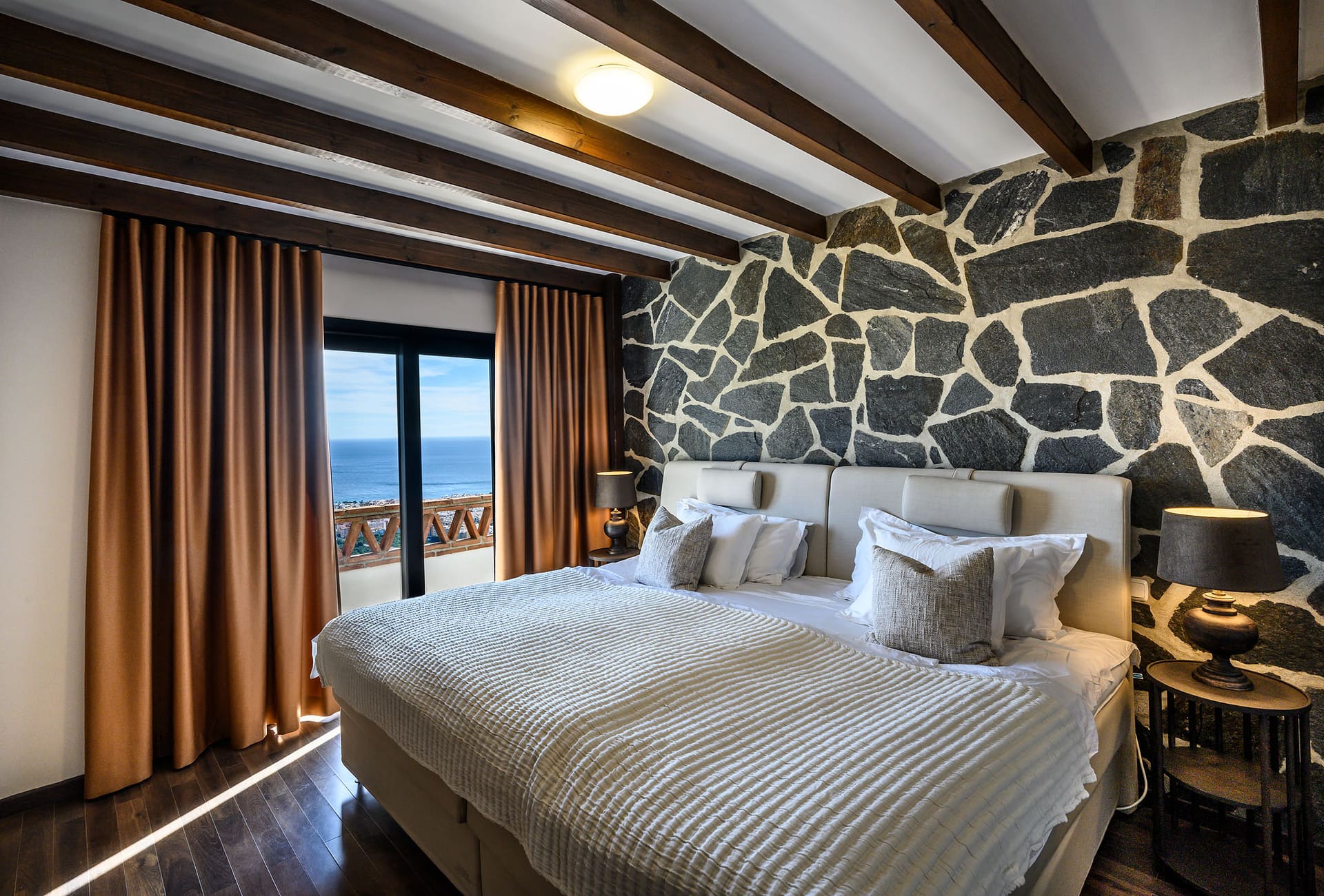 A bedroom at Villa Mango with a natural stone wall and doors onto the terrace.
