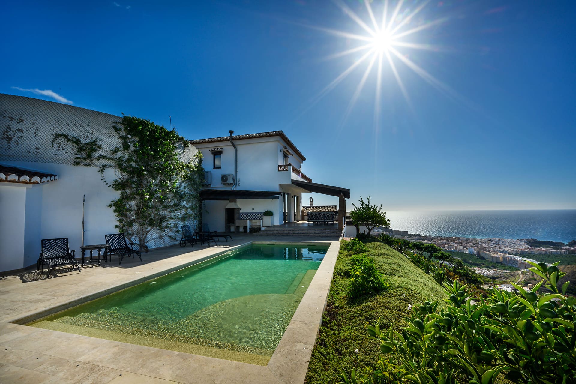 Villa Mango's pool in full sun, the white house behind and Almuñécar and the sea below.