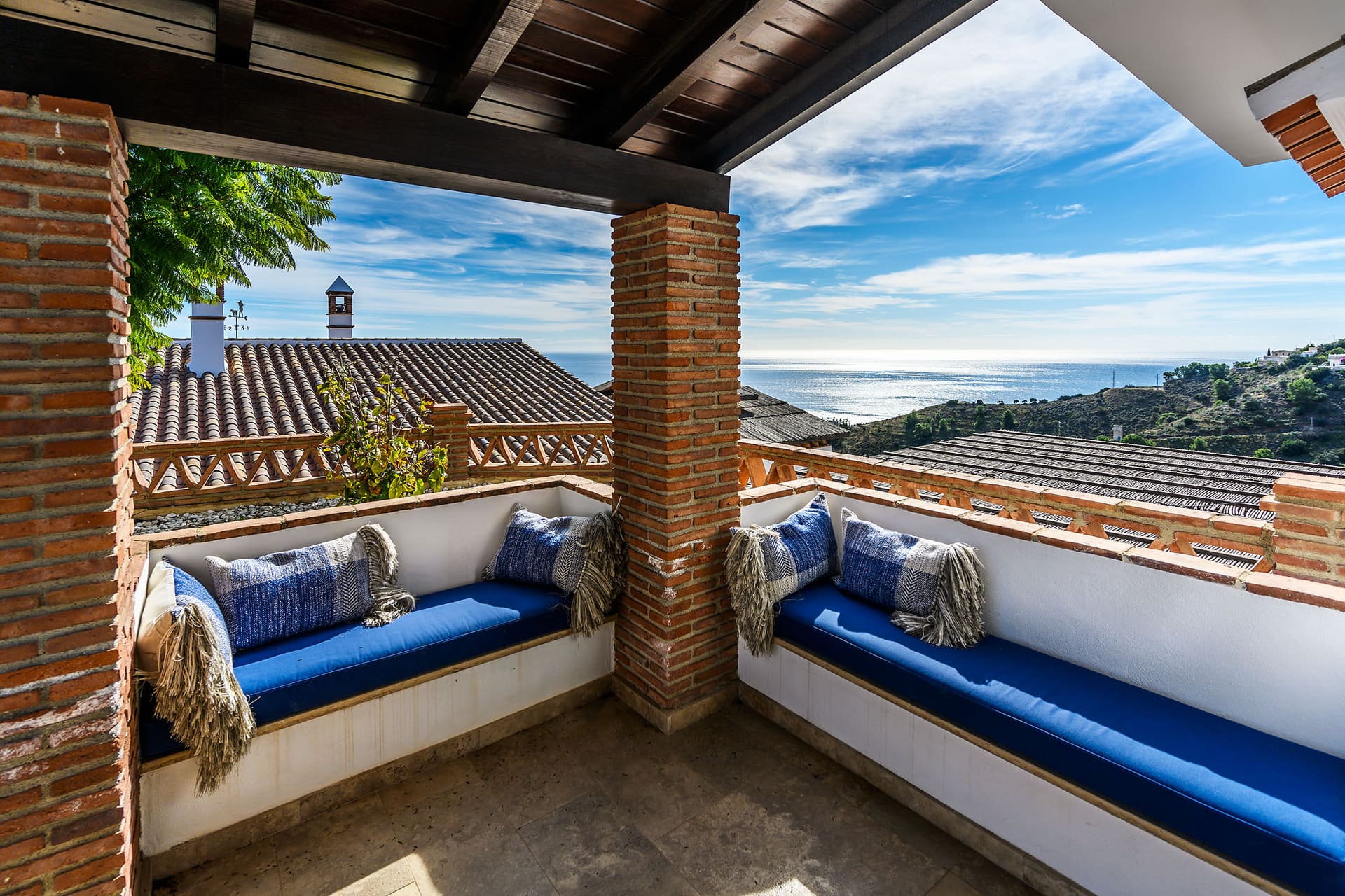 A small tiled terrace with cushioned benches, the rooftops and the sea beyond.