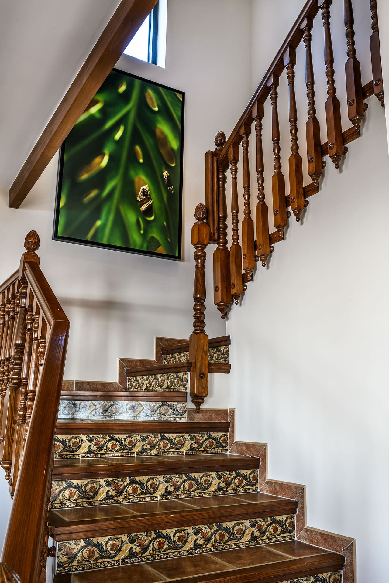 A tiled staircase with a carved wooden banister, a leaf print on the wall.