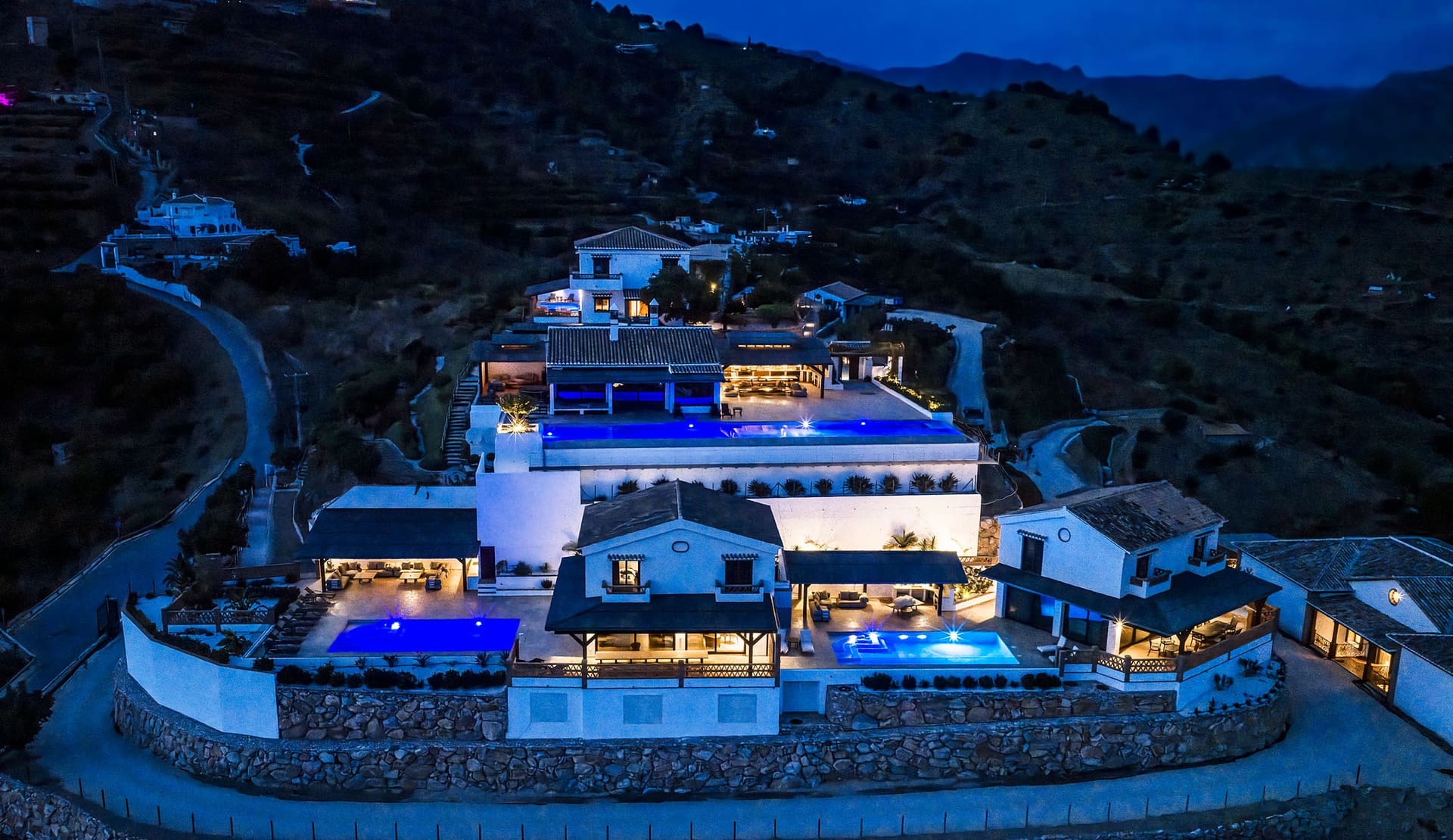 The whole hill and its villas lit up at dusk.