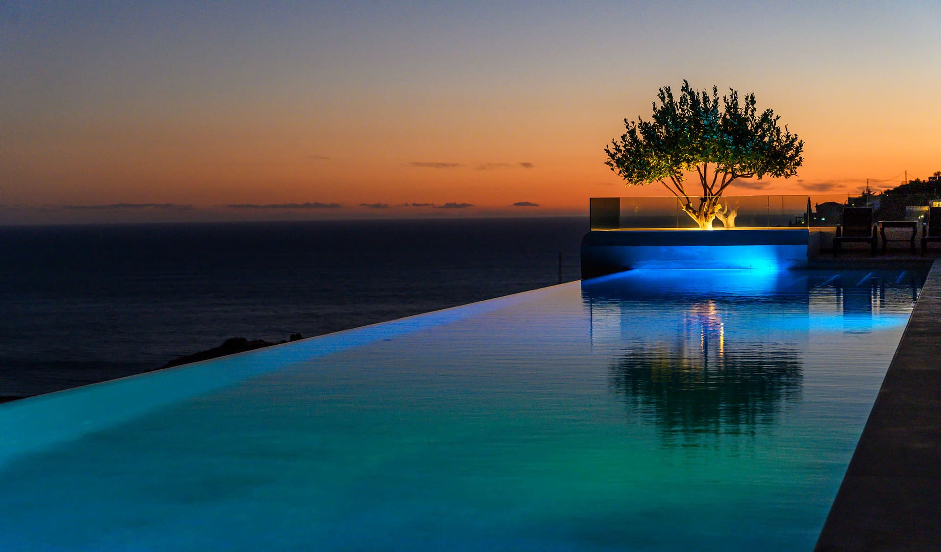 The infinity pool glowing against the sea at dusk.