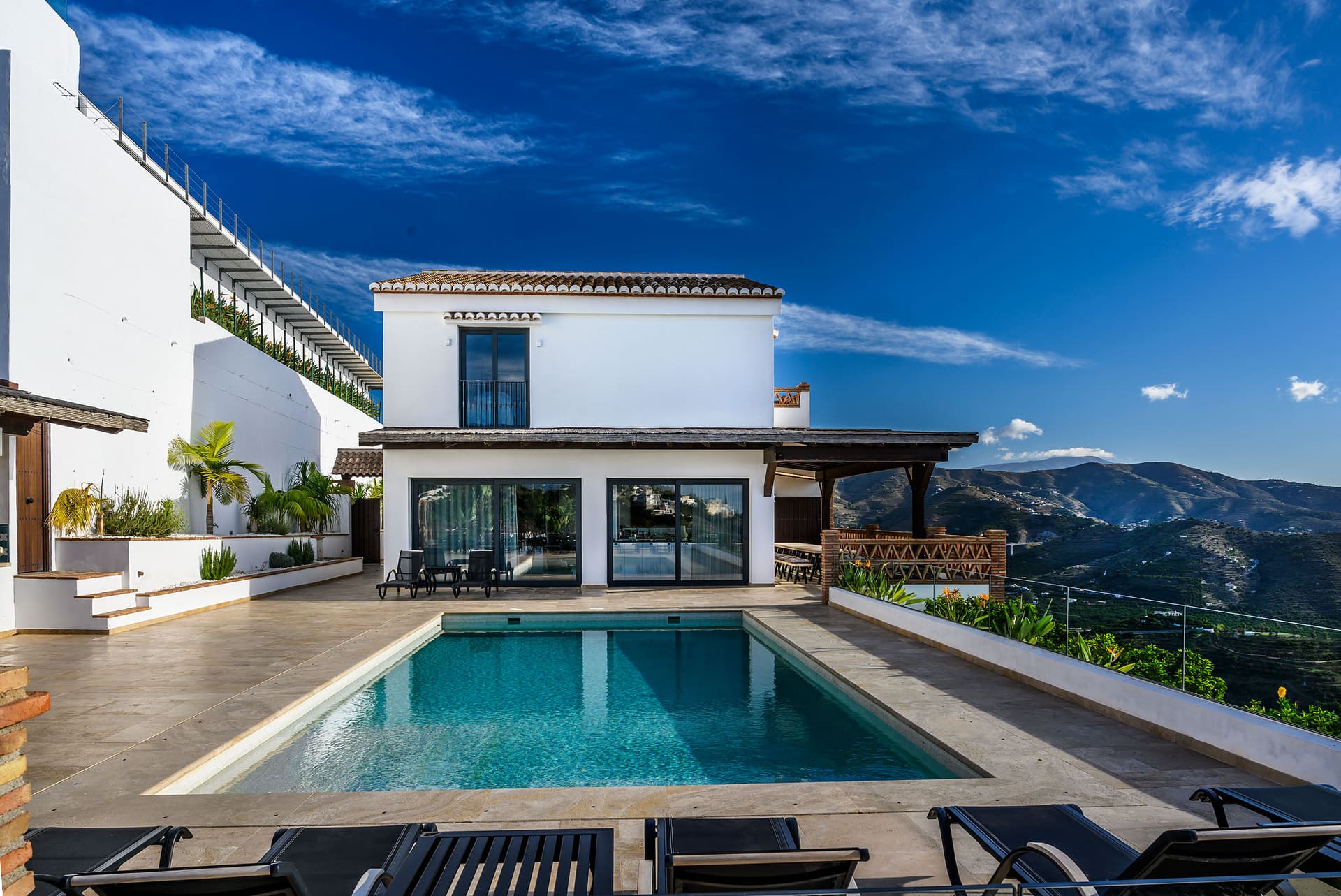 Villa Naranja seen across the pool, white walls against a deep blue sky and the mountains beyond.