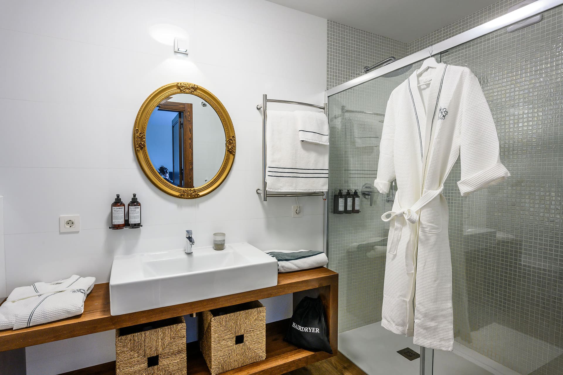 A bathroom at Villa Naranja with a gold-framed mirror, a wooden vanity and a glass shower.