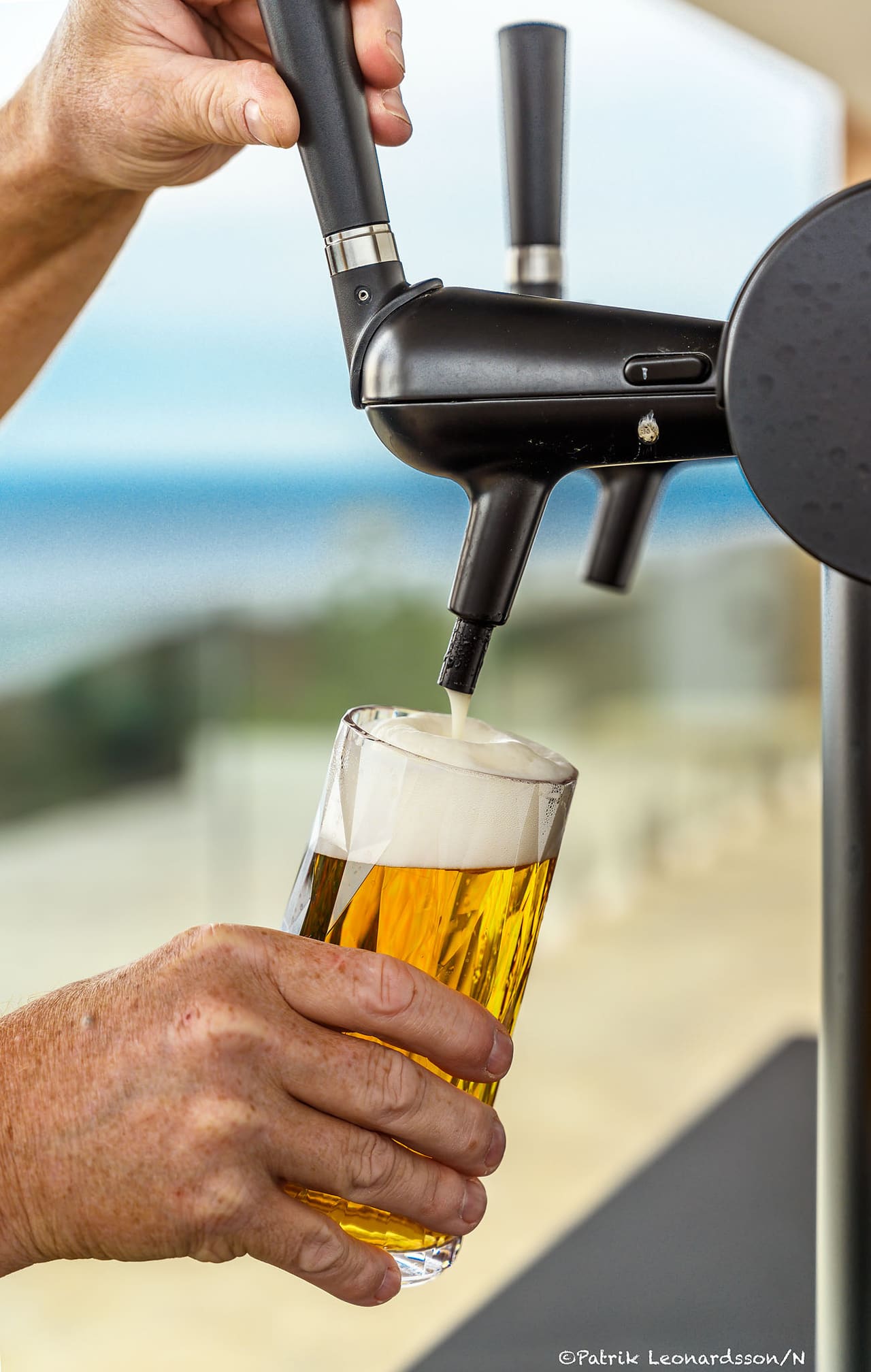 A beer being poured from the mobile bar, the sea blurred behind.