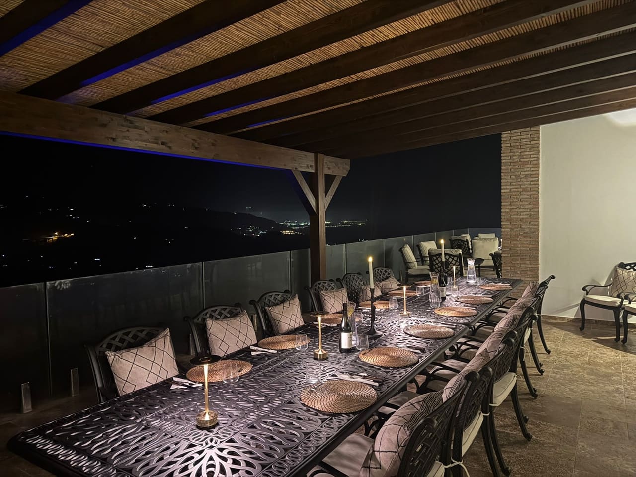 A long table set for dinner on the terrace at night, candles lit.