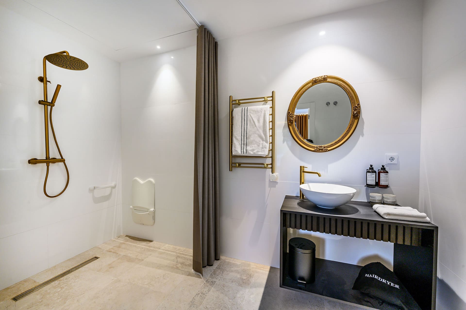 A suite bathroom with a brass rain shower and a round mirror.