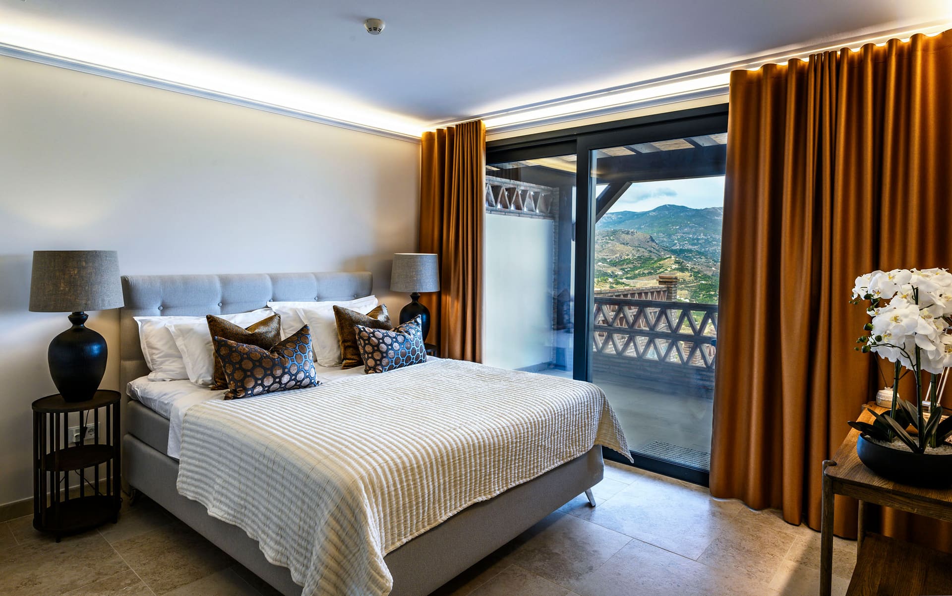 A bright suite bedroom, the mountains framed by the balcony doors.
