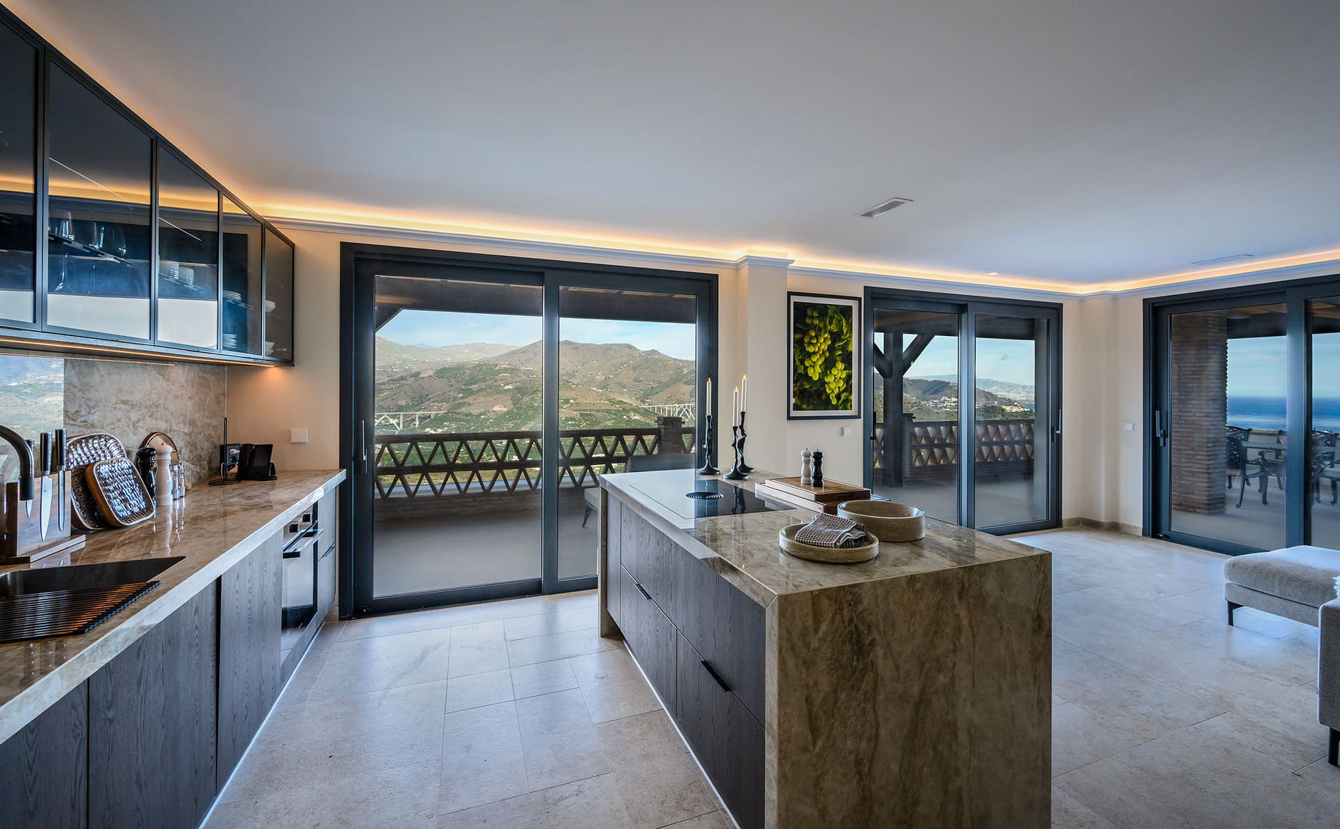 A suite's kitchen with a stone island, glass doors onto the view on two sides.