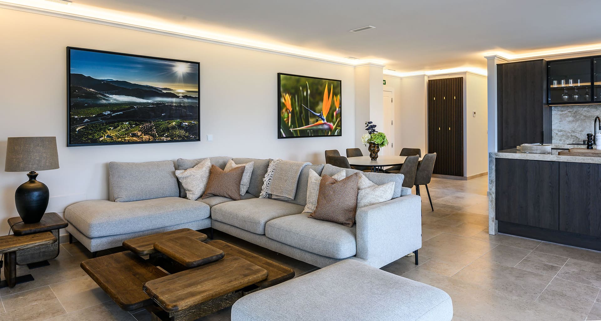 A suite's open living room, a corner sofa, a dining table and the kitchen behind.