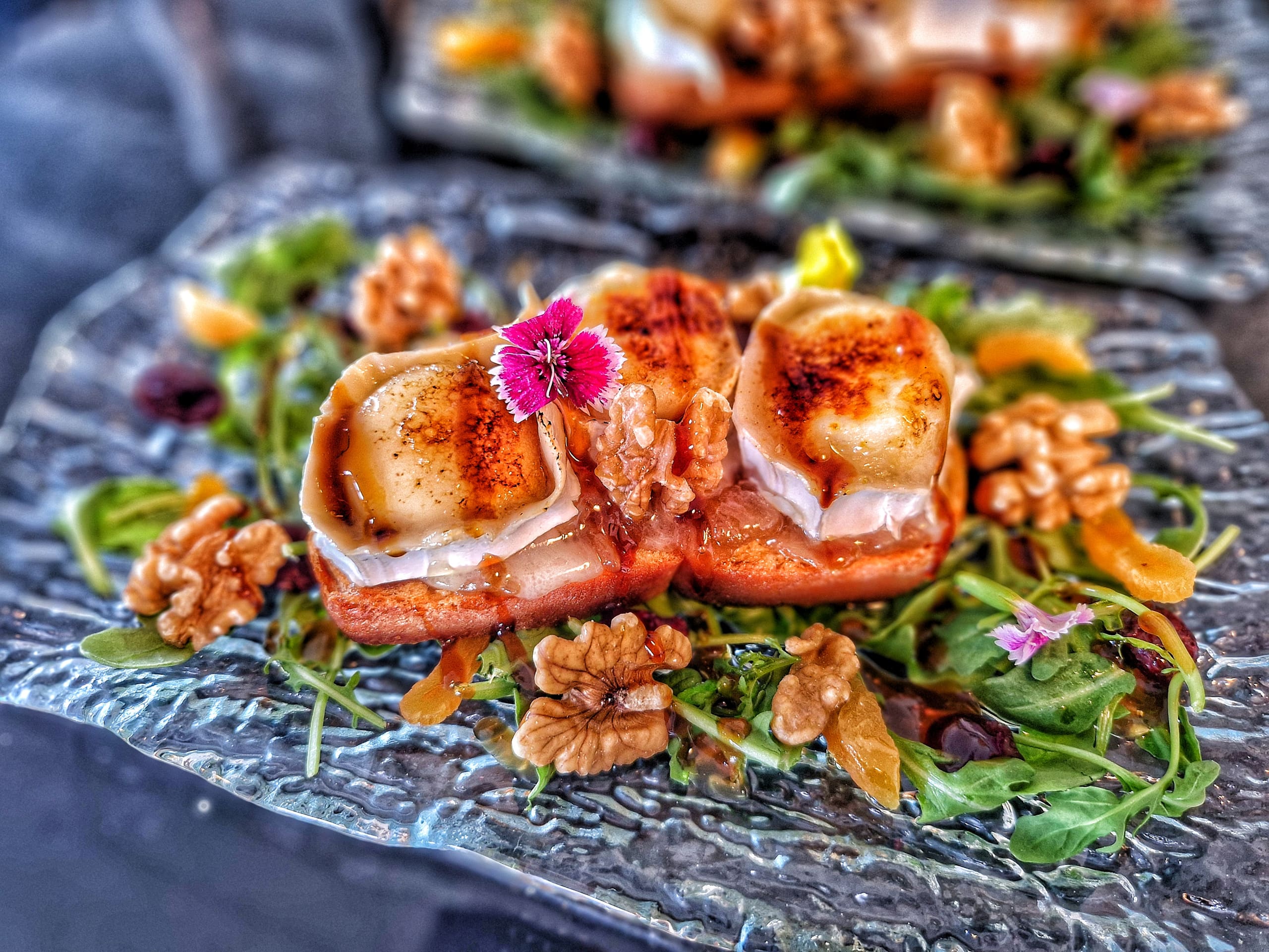 A plated starter of grilled fish on a bed of leaves, finished with edible flowers.