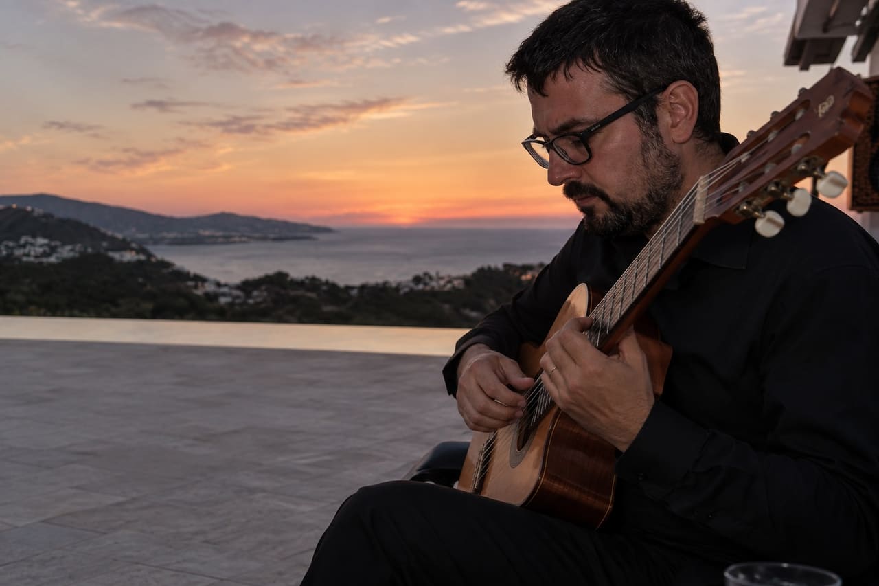 A guitarist playing at sunset, the coast and the sea behind him.
